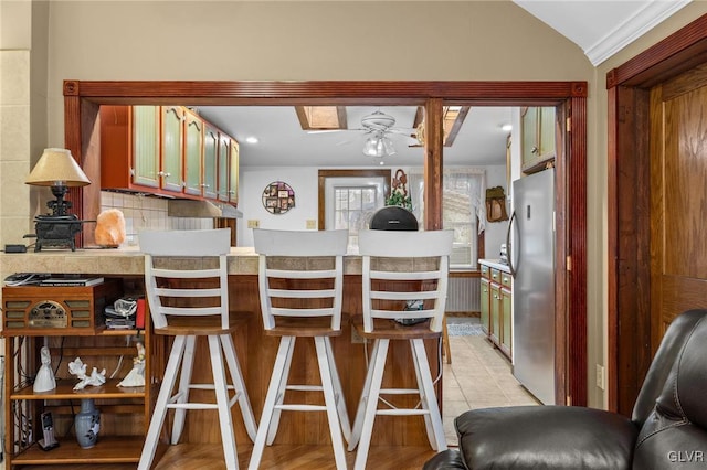 kitchen with lofted ceiling, light tile patterned flooring, ceiling fan, backsplash, and stainless steel fridge