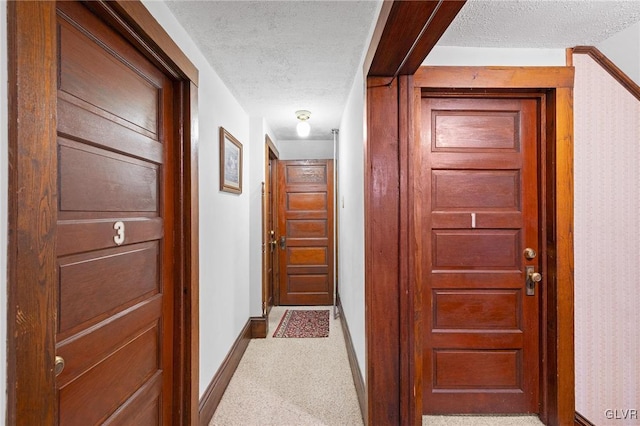 hallway with a textured ceiling and light carpet