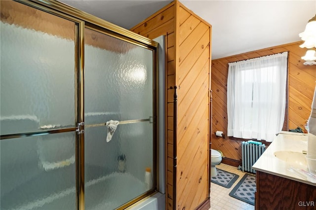 full bathroom featuring radiator heating unit, toilet, bath / shower combo with glass door, wooden walls, and vanity