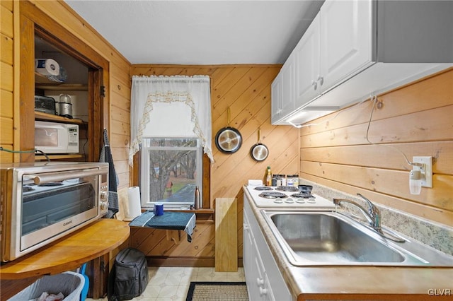 kitchen with wood walls, white appliances, white cabinetry, and sink