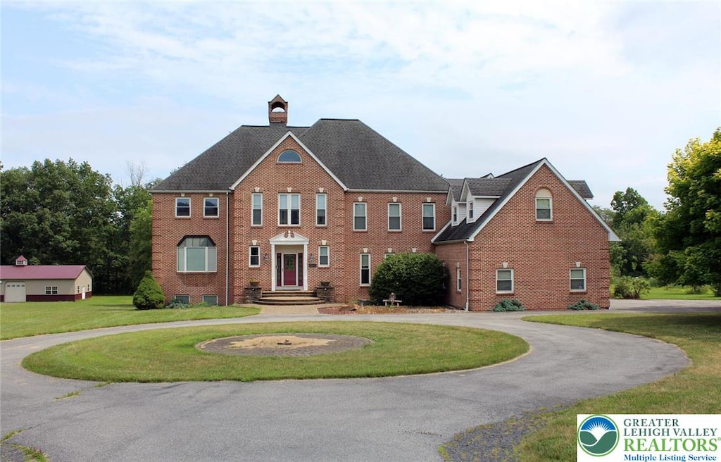 3045 W Scenic Dr, Moore Twp, PA 18038 - colonial home featuring a front yard, curved driveway, brick siding, a chimney, and roof with shingles