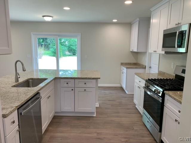 kitchen featuring light stone countertops, stainless steel appliances, sink, light hardwood / wood-style flooring, and white cabinets