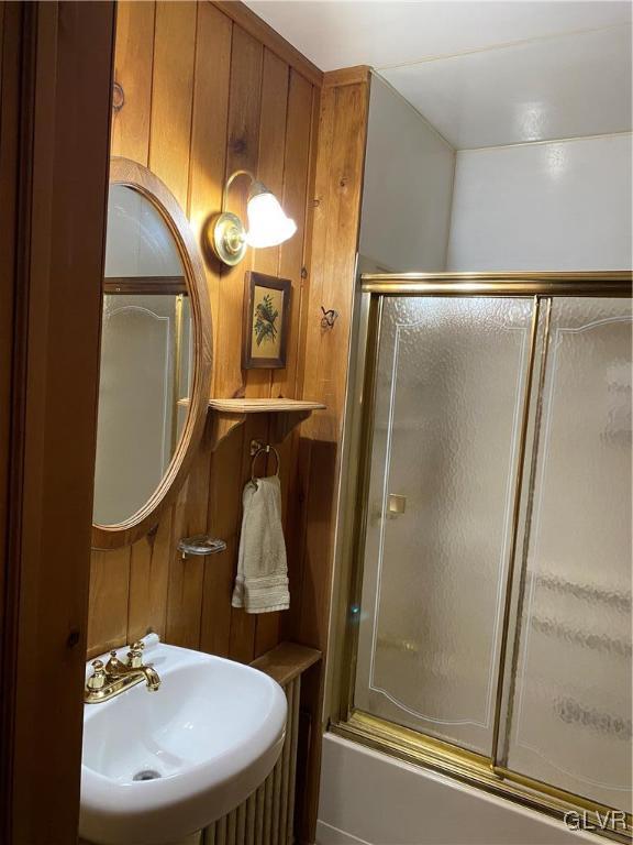 bathroom featuring wooden walls, sink, and bath / shower combo with glass door