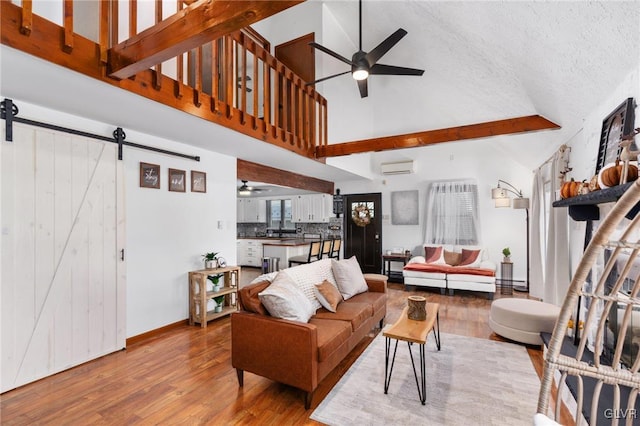 living room featuring a wall mounted air conditioner, a textured ceiling, a barn door, high vaulted ceiling, and hardwood / wood-style floors