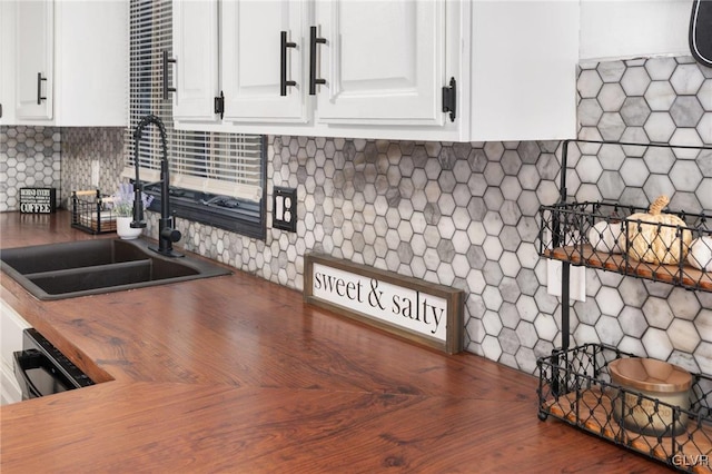 kitchen with butcher block countertops, tasteful backsplash, sink, and white cabinets