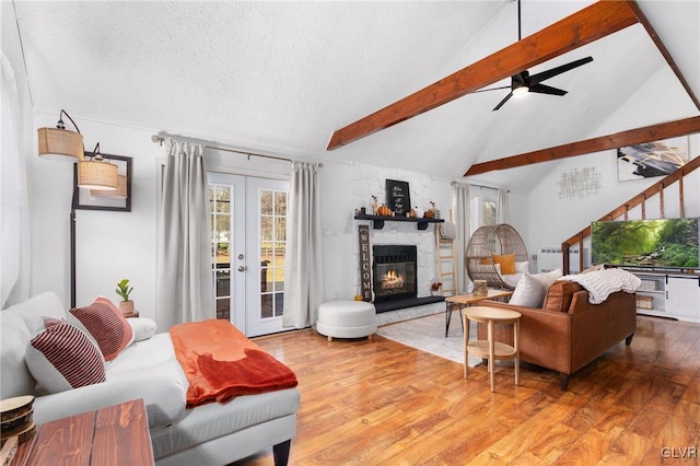 living room featuring hardwood / wood-style floors, french doors, vaulted ceiling with beams, a fireplace, and a textured ceiling