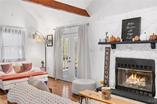 living room featuring wood-type flooring, a stone fireplace, lofted ceiling, and a textured ceiling