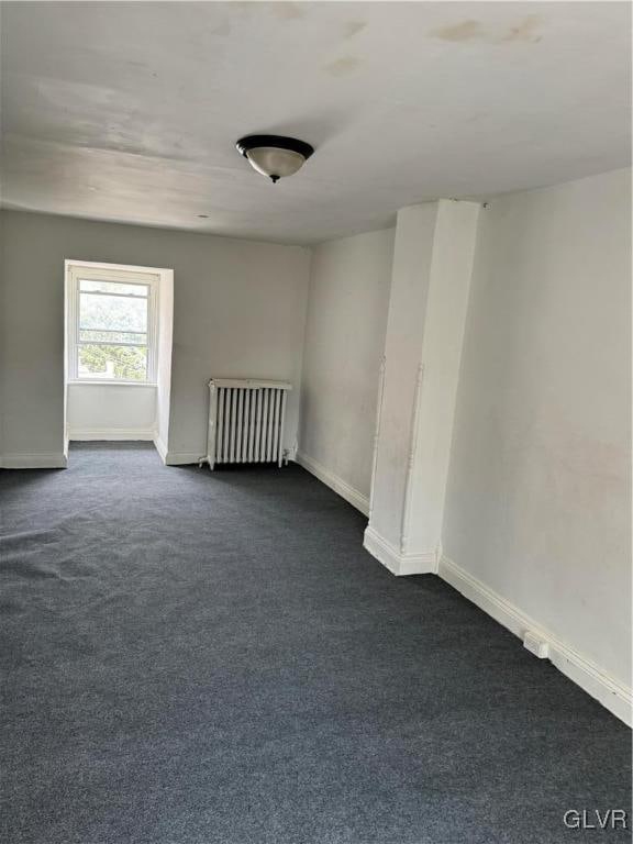 unfurnished room featuring radiator and dark carpet