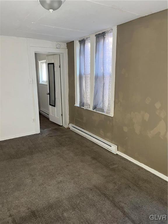 unfurnished room with baseboard heating and dark carpet