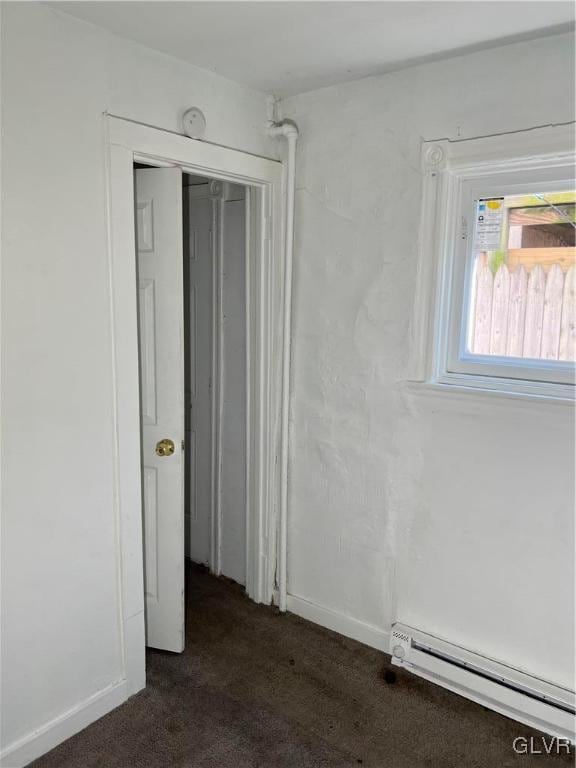 spare room with baseboard heating and dark colored carpet