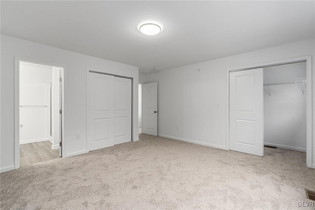 unfurnished bedroom with light carpet, connected bathroom, and multiple closets