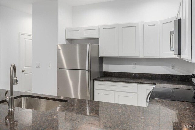 kitchen featuring white cabinets, appliances with stainless steel finishes, dark stone countertops, and sink