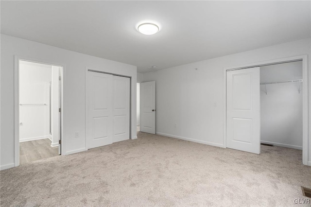 unfurnished bedroom with visible vents, baseboards, ensuite bathroom, carpet, and two closets