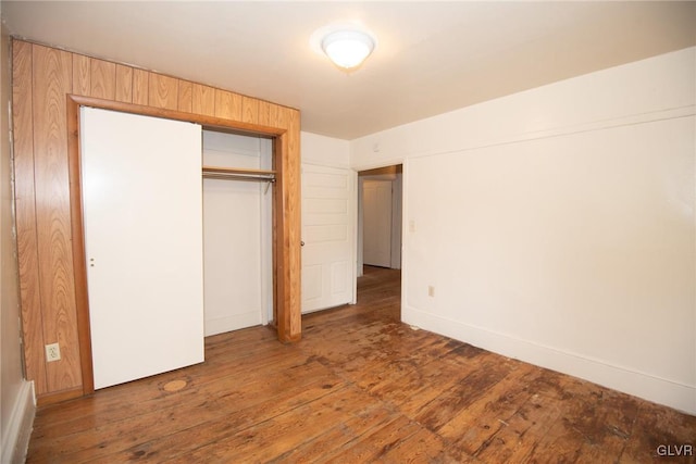 unfurnished bedroom featuring wooden walls, a closet, and dark wood-type flooring