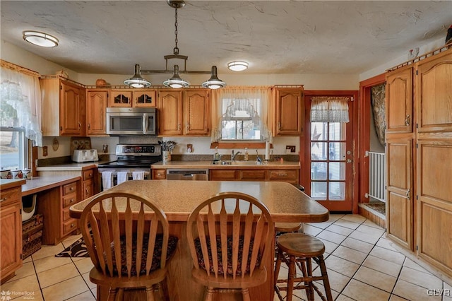 3479 Mango Dr, Lehigh Township, PA 18038 - kitchen with stainless steel appliances, light tile patterned floors, a kitchen island, a breakfast bar area, and brown cabinetry