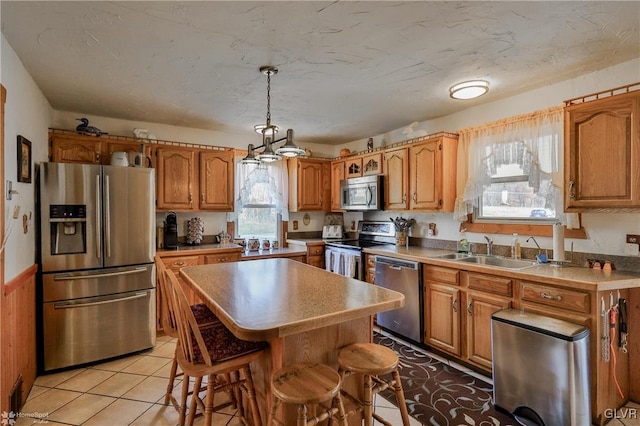 kitchen with sink, a kitchen island, pendant lighting, light tile patterned flooring, and appliances with stainless steel finishes