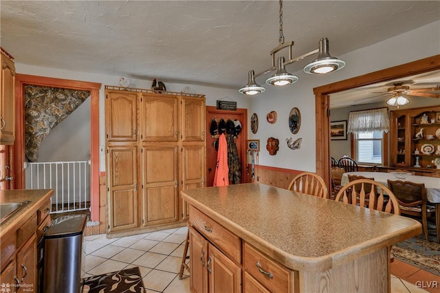 3479 Mango Dr, Lehigh Township, PA 18038 - kitchen featuring light tile patterned flooring, ceiling fan, a wainscoted wall, a center island, and brown cabinets