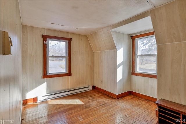 additional living space with wood walls, light hardwood / wood-style floors, lofted ceiling, and a baseboard radiator