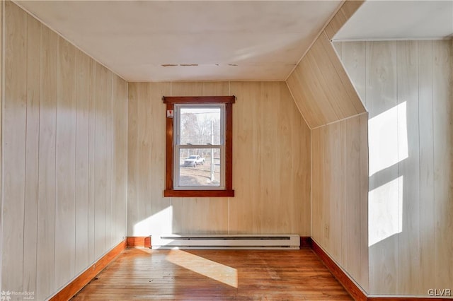 additional living space with light wood-type flooring, wooden walls, and a baseboard heating unit