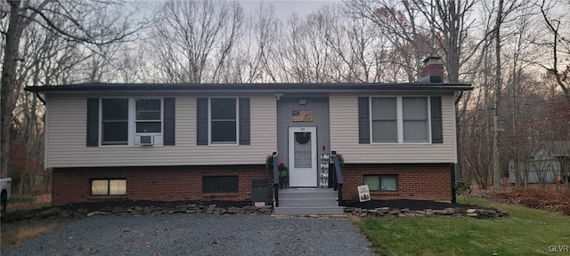 raised ranch with brick siding, a chimney, and a front yard