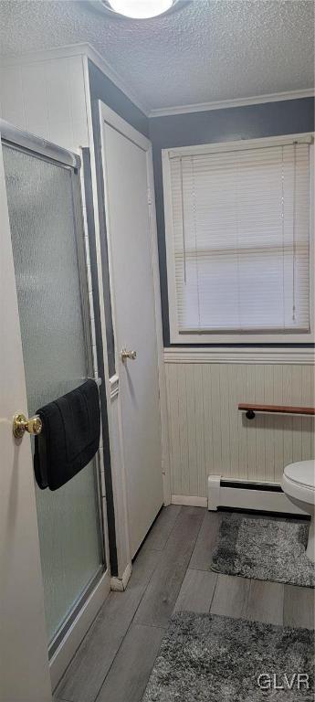 full bathroom featuring wood finish floors, a shower stall, a textured ceiling, and baseboard heating