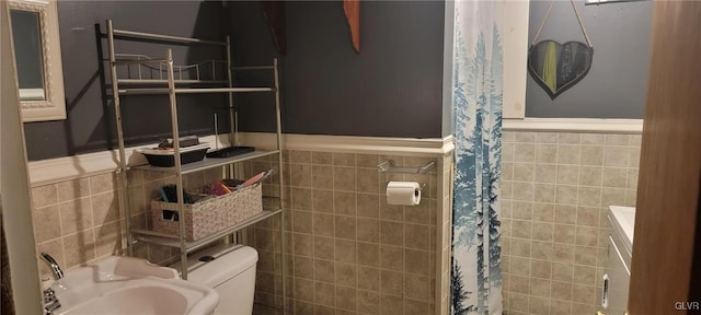 bathroom featuring a wainscoted wall, a sink, tile walls, and toilet