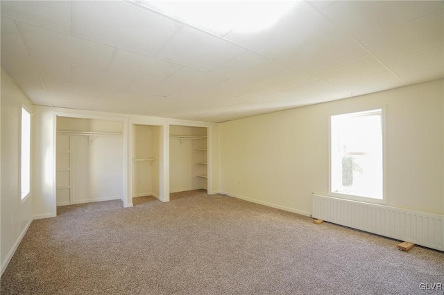 unfurnished bedroom featuring carpet flooring, radiator, and two closets