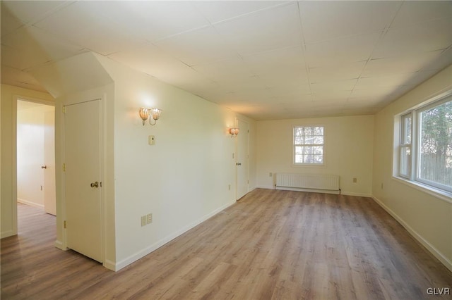 unfurnished room featuring plenty of natural light, radiator, and light hardwood / wood-style flooring