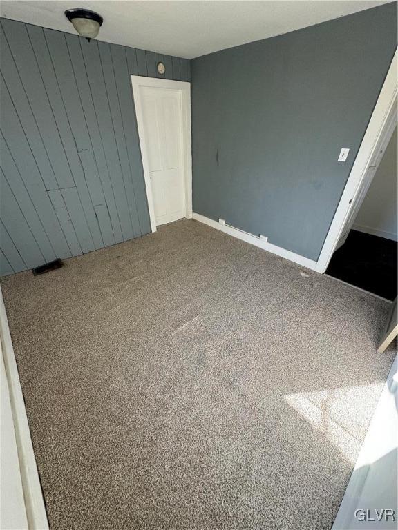 unfurnished bedroom featuring carpet and wood walls