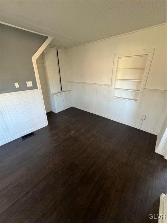 spare room with built in shelves and dark hardwood / wood-style flooring