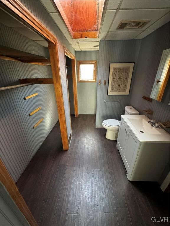 bathroom with a paneled ceiling, vanity, wooden walls, wood-type flooring, and toilet