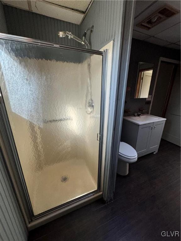 bathroom with a drop ceiling, vanity, hardwood / wood-style flooring, toilet, and a shower with shower door