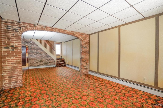 interior space with carpet flooring, a paneled ceiling, a baseboard heating unit, and brick wall