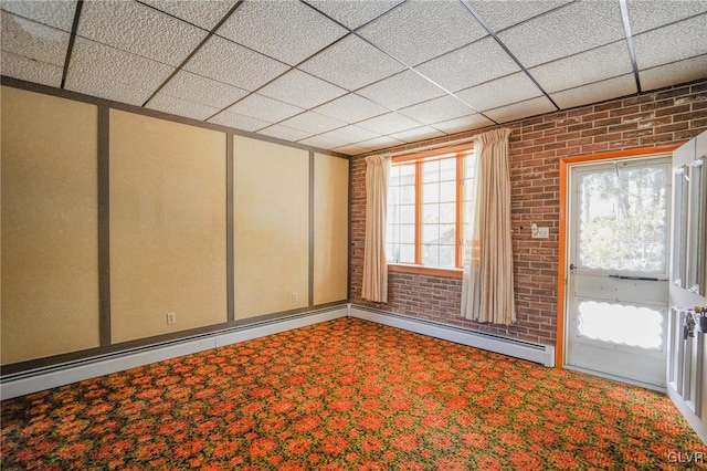 empty room featuring baseboard heating, a paneled ceiling, carpet, and brick wall