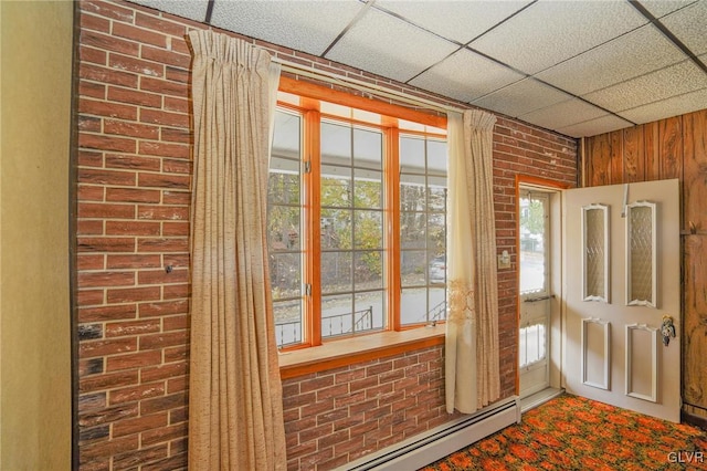 doorway to outside with plenty of natural light, a drop ceiling, and brick wall