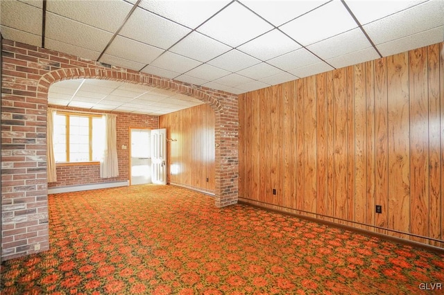 unfurnished living room with wooden walls, a paneled ceiling, and brick wall