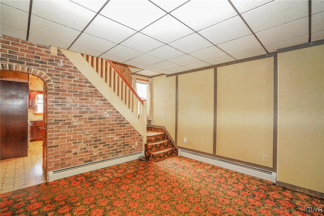 basement with baseboard heating, a paneled ceiling, and brick wall