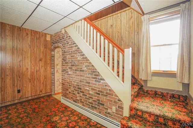 stairs featuring wooden walls, plenty of natural light, and a baseboard heating unit