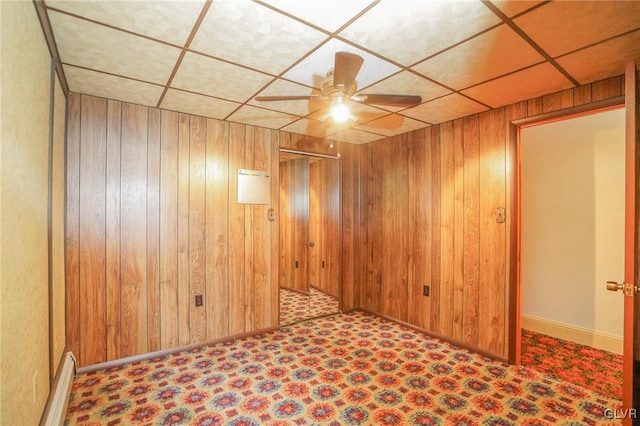 basement featuring a paneled ceiling, ceiling fan, and wooden walls