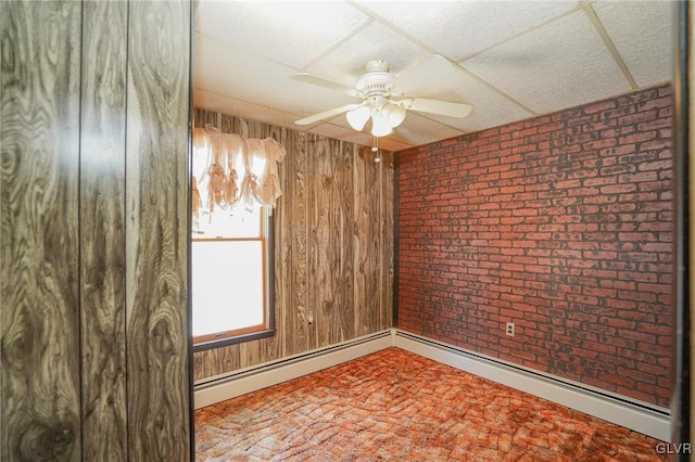 spare room with ceiling fan, wood walls, a drop ceiling, and brick wall