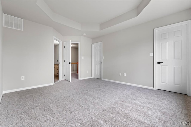 unfurnished bedroom featuring a raised ceiling, ensuite bath, and light carpet