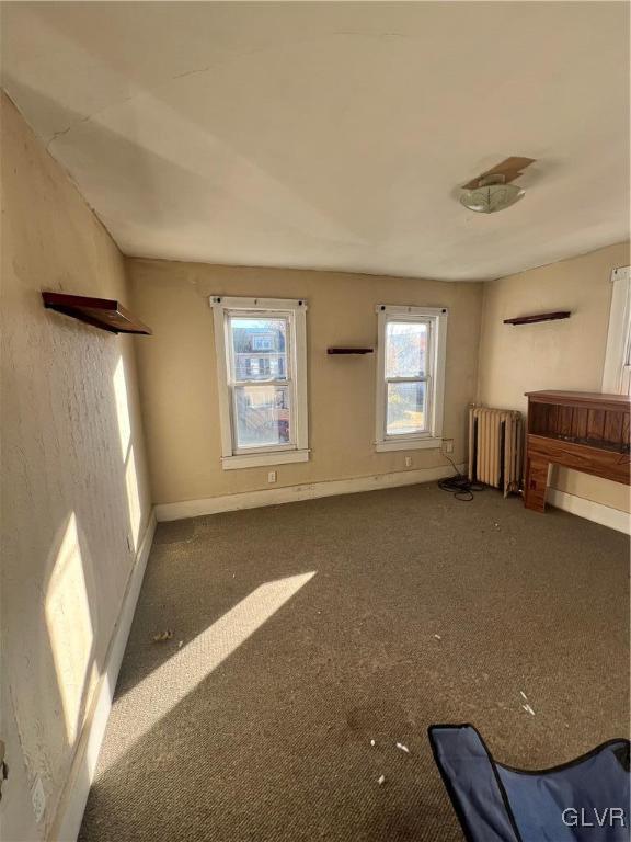 unfurnished living room with radiator and dark carpet