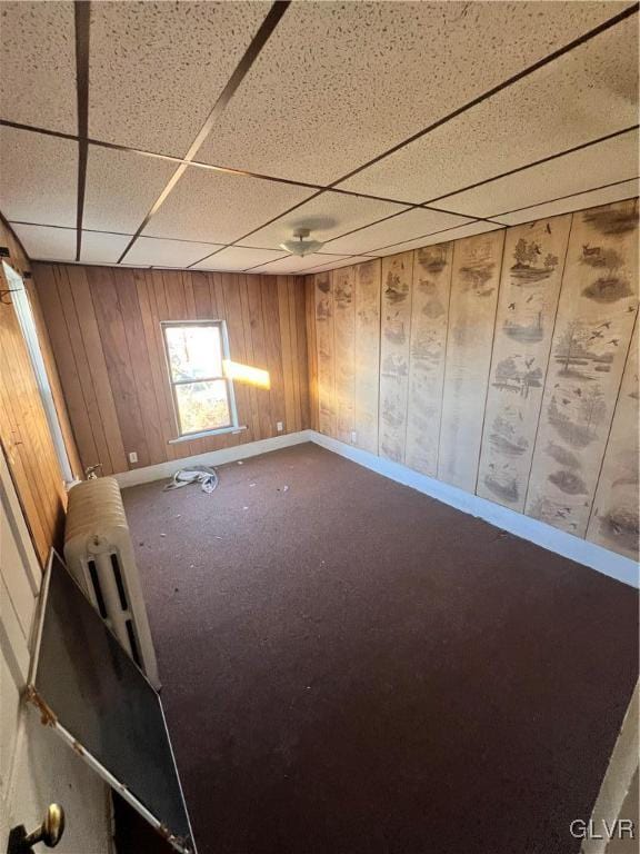 empty room featuring carpet flooring, a paneled ceiling, and wooden walls