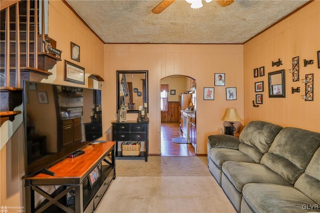 living room with ceiling fan, wooden walls, and a textured ceiling