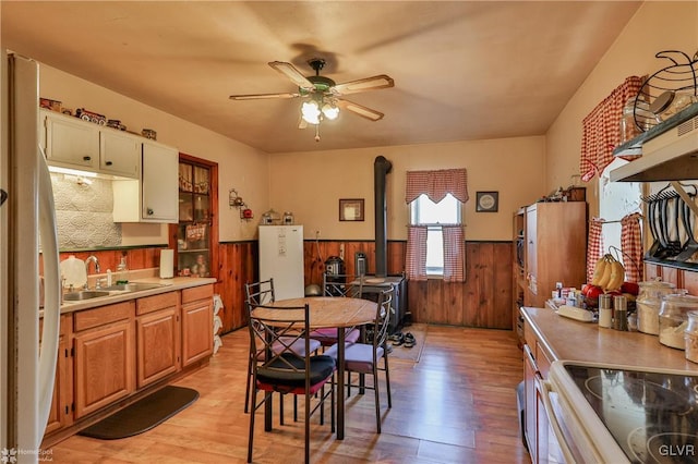 dining room featuring light wood-type flooring, sink, wooden walls, and a wood stove