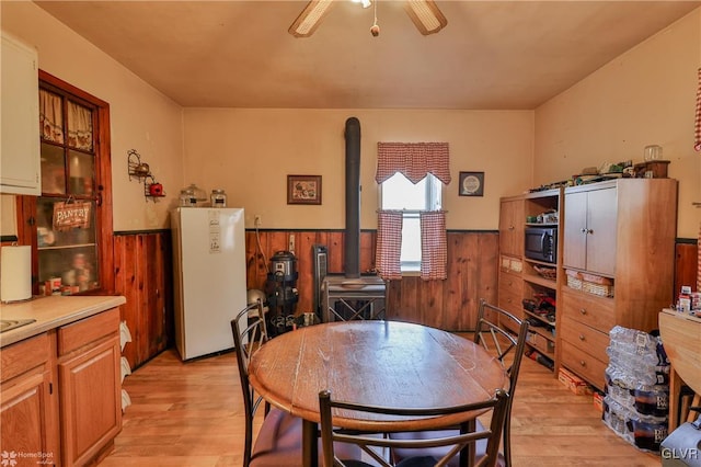 dining area featuring ceiling fan, wood walls, and light wood-type flooring