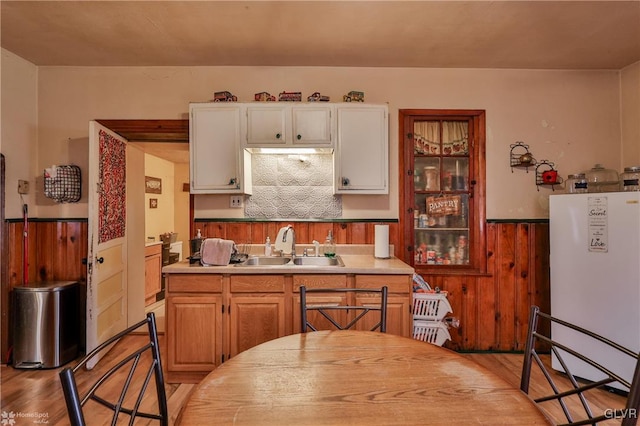 kitchen featuring light wood-type flooring, white refrigerator, wood walls, and sink