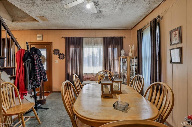 dining room featuring carpet, ceiling fan, a textured ceiling, and wooden walls