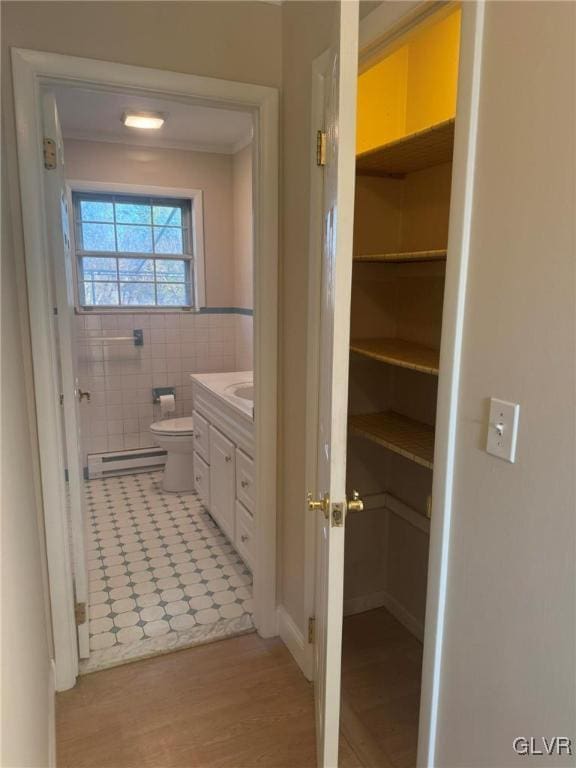 bathroom with a baseboard radiator, toilet, vanity, tile walls, and hardwood / wood-style flooring