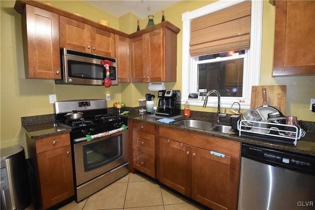 kitchen featuring light tile patterned flooring, appliances with stainless steel finishes, dark stone counters, and sink